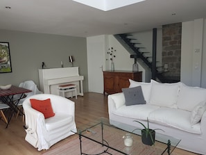 A modern living room with a piano, white sofas, a glass coffee table, and a staircase with a stone wall.