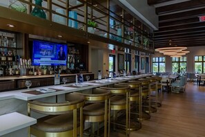 A bar area with a long counter, multiple stools, and a television screen displaying news. - 9BR Solara Villa | Rare Private Lot, Pool & Jacuzzi, Game Room | Dog Friendly (Kissimmee)