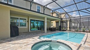 Une piscine avec un jacuzzi, entourée d’une terrasse couverte donnant sur le jardin.