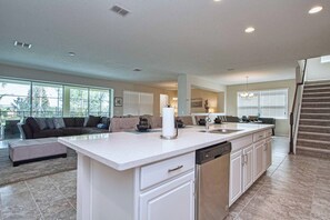 A spacious living area with a large window, a kitchen with a central island, and a staircase leading to another level. - 9BR Solara Villa | Rare Private Lot, Pool & Jacuzzi, Game Room | Dog Friendly (Kissimmee)