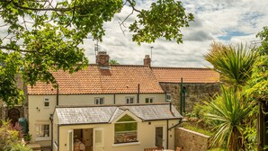 A two-story house with a tiled roof, a small attached garage, and a garden with a patio.