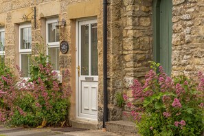 A stone building with a white door and windows, surrounded by pink flowering plants. - Beadale Cottage, Ampleforth, North York Moors (Ampleforth)