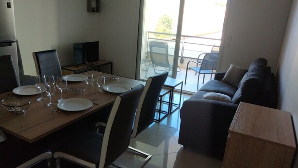 Un comedor con una mesa de madera dispuesta para cuatro personas, sillas alrededor y un sofá al fondo.