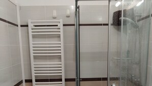 Un baño con cabina de ducha de vidrio, un lavabo blanco y un perchero para toallas.