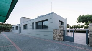 A modern building with a flat roof, large windows, and a stone wall. - Αmfithea Villas (Πετροκεφάλι)