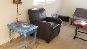 Una habitación con una mesita de noche azul, un sillón de cuero marrón y un sofá gris.