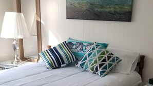 Una cama bien tendida con ropa blanca, cabecera de madera y varios almohadones con diseños geométricos.
