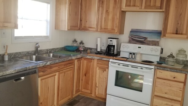 Una cocina con armarios de madera, lavavajillas, estufa, cafetera y ventana.