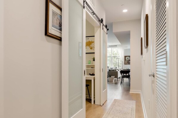 A hallway with a sliding door leading to a dining area, a white door with blinds, and a framed picture on the wall.