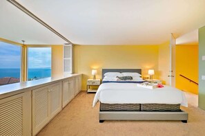 A bedroom with a bed, bedside lamps, a nightstand, a window with a view, and a door.