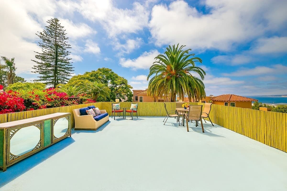 An outdoor patio with a sofa, chairs, and a table, surrounded by a yellow fence and various plants.