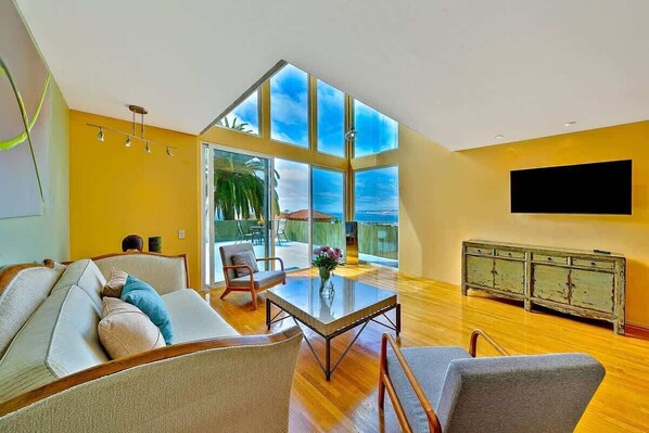 A spacious living room with a large glass window, a flat-screen TV, and a wooden cabinet.