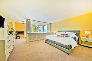 Habitación de hotel con cama, cómoda, tocador con espejo, escritorio y ventana con vista a palmeras.