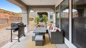 En overdækket terrasse med grill, udendørs møbler og udsigt over ørkenlandskabet.