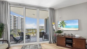 Ein geräumiges Wohnzimmer mit Balkon, einem großen Strandbild und einem Holzkabinett.
