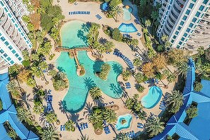 An aerial view of a resort with multiple swimming pools, palm trees, and lounge areas.