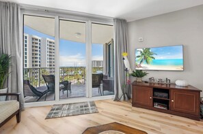 A spacious living room with a balcony, a large painting of a beach, and a wooden cabinet.