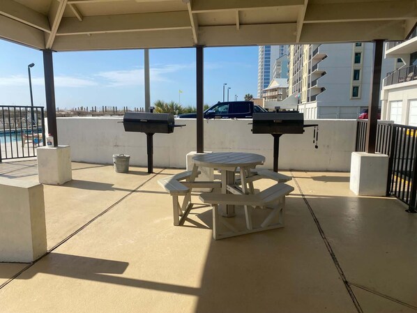 Un espace extérieur aménagé en terrasse, avec une table ronde et deux barbecues.