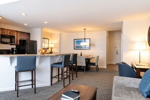 A modern hotel room with a kitchenette, a dining area, and a living space.