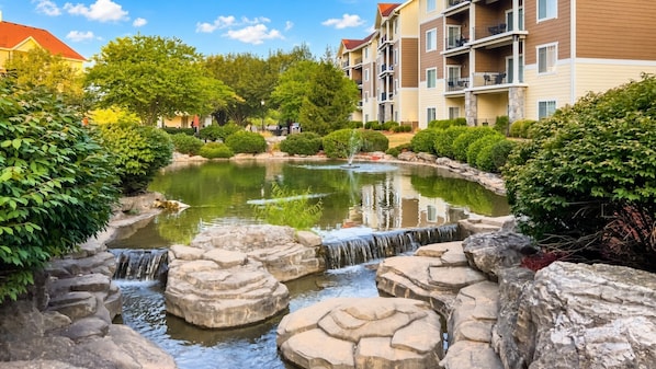A residential area with a pond, a small waterfall, and multi-story buildings with balconies.