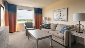 A hotel room with a sofa, armchair, and a small table. There is a window with curtains, a lamp, and a painting on the wall. - Miramar Beach | Couples Golf & Beach Trip | Pool + Golf (Miramar Beach)