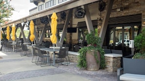 An outdoor patio with tables and chairs, yellow umbrellas, and potted plants.
