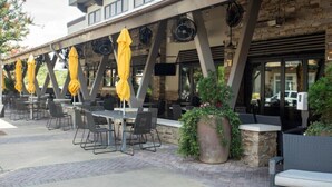 An outdoor patio with tables and chairs, yellow umbrellas, and potted plants.