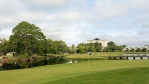 A golf course with a pond, trees, and a building in the background.