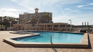 A swimming pool with multiple lanes, a covered seating area, and a building with a distinctive tower in the background.