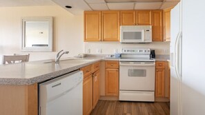 A compact kitchen with wooden cabinets, a microwave, an oven, and a dishwasher. - Miramar Beach | Couples Golf & Beach Trip | Pool + Golf (Miramar Beach)