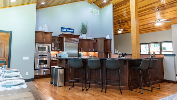 A spacious kitchen with wooden cabinets, a stainless steel refrigerator, and a bar area with stools. - Perfect getaway for large families who love the woods and beach!! (Woodbine)