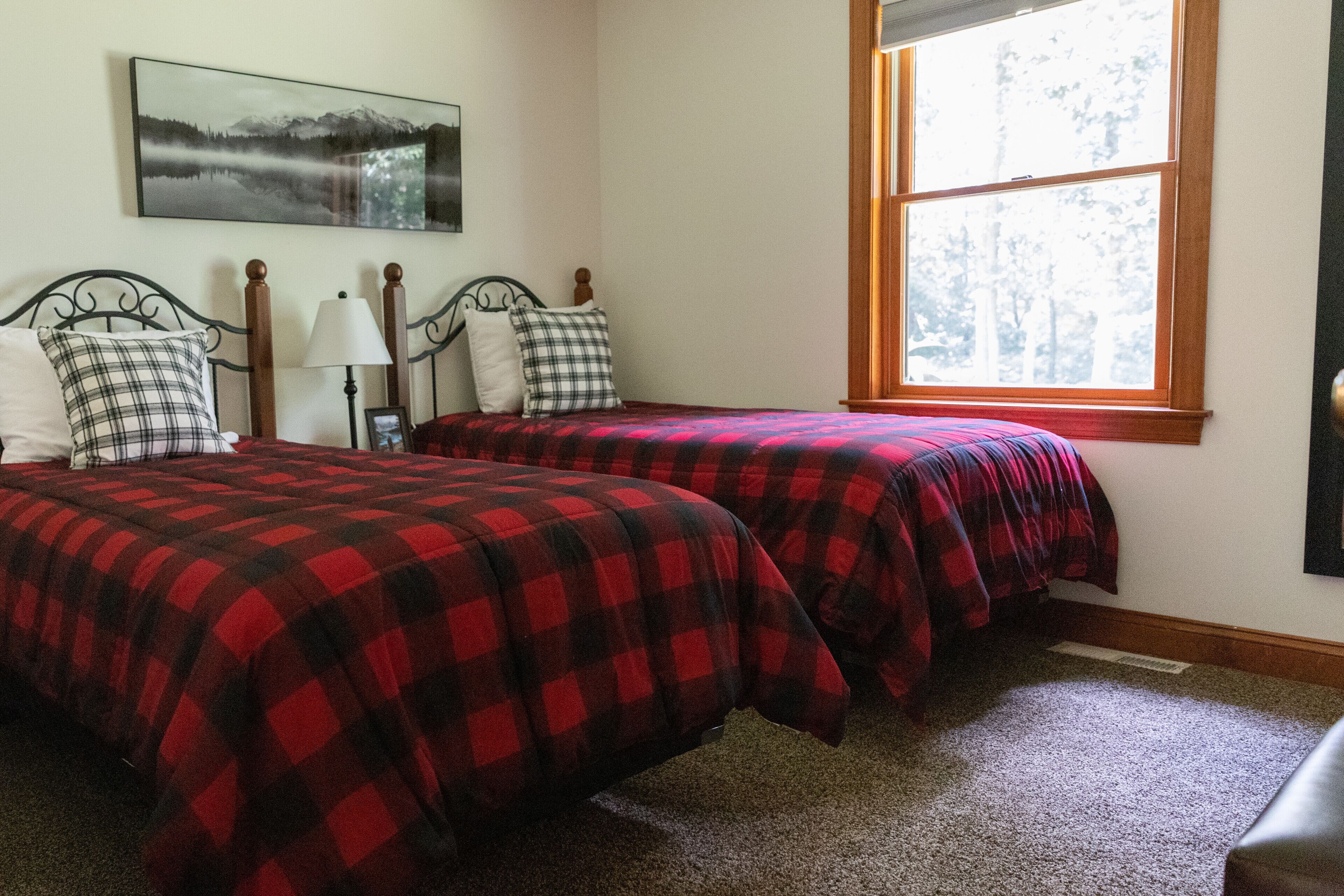 A bedroom with two beds, a nightstand, a lamp, and a window with a view of trees.