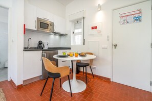 A compact kitchen with a microwave, stove, and sink, a dining table with chairs, and a tiled floor.