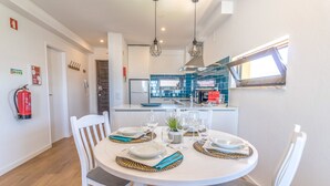 A modern kitchen with blue tiles, a dining area with a white table set for four, and a fire extinguisher on the wall. - #063 Beach Flat by Home Holidays (Albufeira)