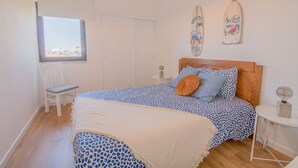 A bedroom with a bed, a chair, a nightstand, a lamp, and a window. - #063 Beach Flat by Home Holidays (Albufeira)