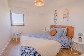 A bedroom with a bed, a chair, a nightstand, a lamp, and a window.