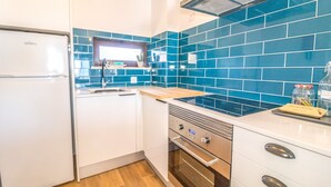 A modern kitchen with a white refrigerator, stainless steel appliances, and blue-tiled backsplash. - #063 Beach Flat by Home Holidays (Albufeira)