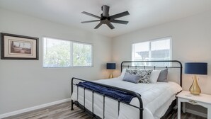 Une chambre à coucher comprenant un lit, deux tables de chevet, un ventilateur de plafond et deux fenêtres.