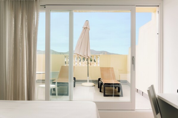 A hotel room with a sliding glass door leading to a balcony with a table, chairs, and an umbrella. - Bluesea Paraiso Beach (Santa Eulalia del Rio)