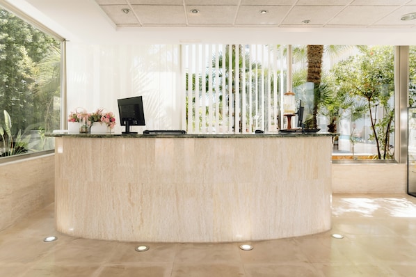 A reception desk with a computer, a vase of flowers, and a potted plant. - Bluesea Paraiso Beach (Santa Eulalia del Rio)