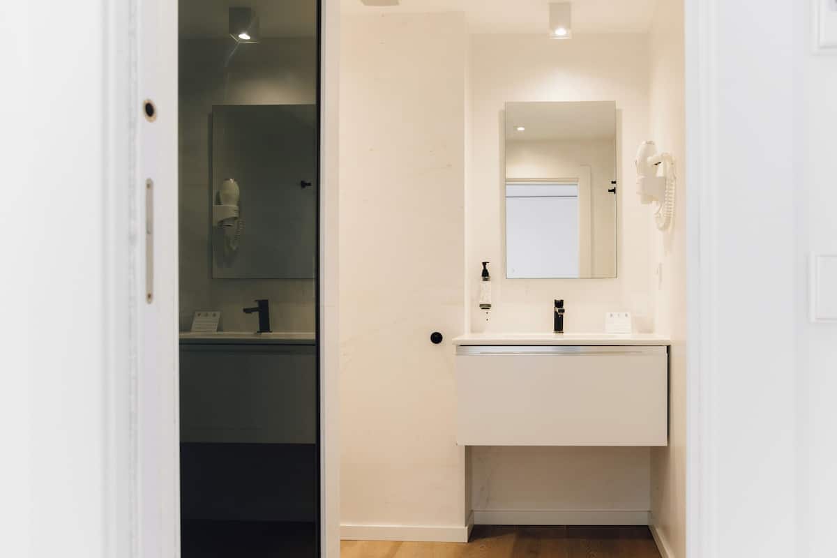 A modern bathroom with a white sink, mirror, and hairdryer mounted on the wall.