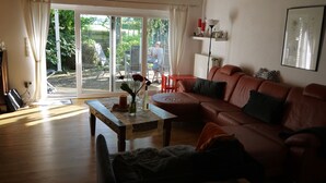 A living room with a brown leather sofa, a wooden coffee table, and a view of a garden through a sliding glass door. - Ferienhaus am Dümmer (Hüde)