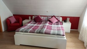A bedroom with a bed, a red armchair, a white bedside table, and a red wall. - Ferienhaus am Dümmer (Hüde)