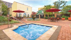 A hot tub surrounded by outdoor seating with red umbrellas, a brick patio, and a fountain. - Guacamole Sunset (CaptainCook)