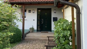 A two-story house with a tiled roof, a green door, and a small porch with a bench.