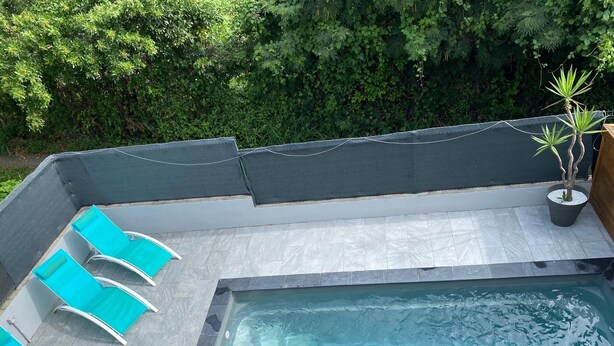 En pool på taget med et glashegn, omgivet af et mørkt tag og en fliseterrasse.