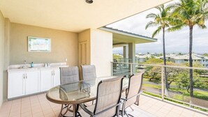 Ein Balkon mit Glastisch und Stühlen, eine Küchenzeile mit weißen Schränken sowie Blick auf Palmen und Gebäude.