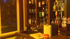 A bar area with shelves of bottles and glasses, a window, and a stained glass ceiling.
