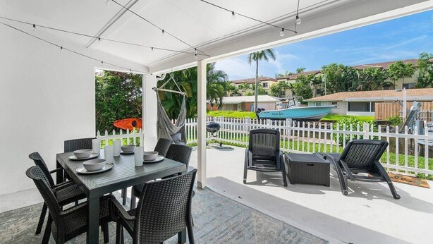 Une terrasse couverte avec une table et des chaises, un hamac et une vue sur une piscine et des maisons.