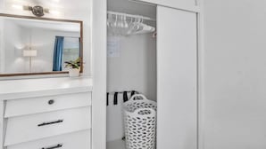 Une salle de bain blanche avec un miroir, un lavabo, une plante en pot, un porte-serviettes suspendu et un panier à linge.